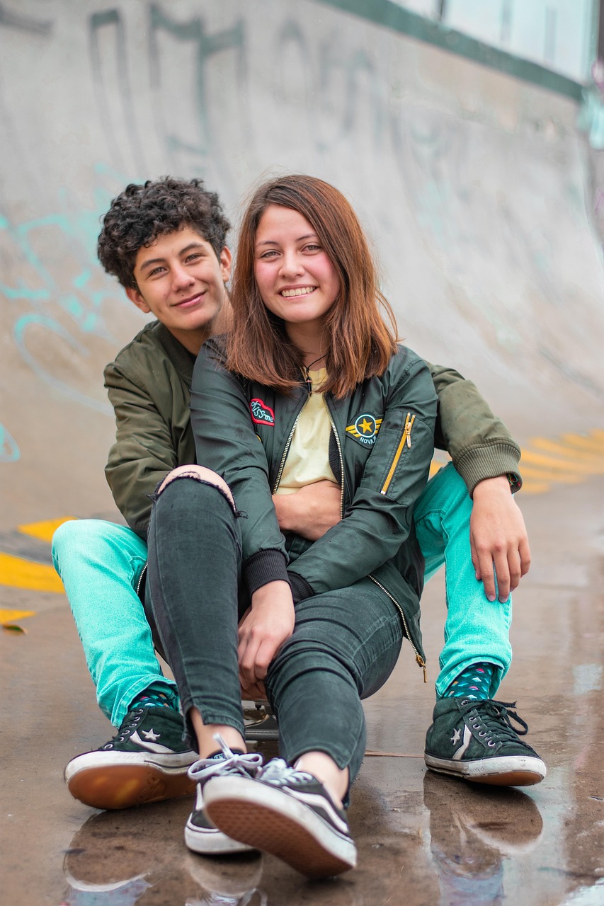 Zwei junge Menschen in einer Beziehung sitzen auf einem Skateboard und lächeln in die Kamera